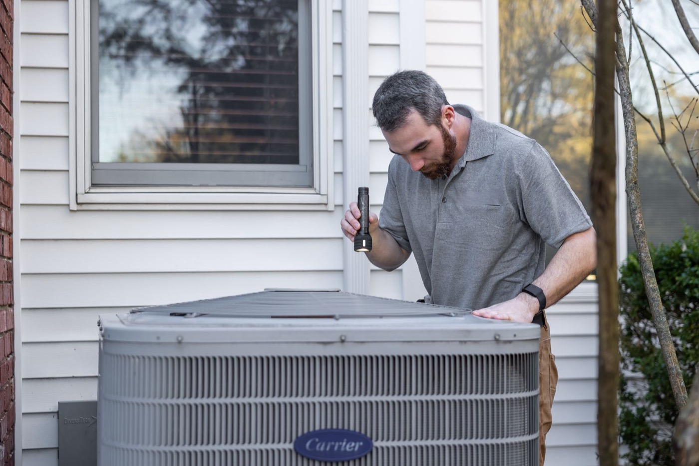 HVAC technician inspecting an outdoor air conditioning condenser at a home